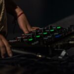 Un close-up sur un contrôleur musical avec des boutons lumineux de couleurs vertes et rouges, manipulé par une main, avec des câbles connectés à l'appareil.