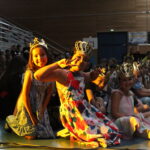 Quatre enfants portant des couronnes, assis en souriant pendant un événement, avec d'autres enfants en arrière-plan.